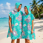 Poncho serviette a capuche motif paresseux turquoise, porte par un couple souriant sur une plage de sable fin.