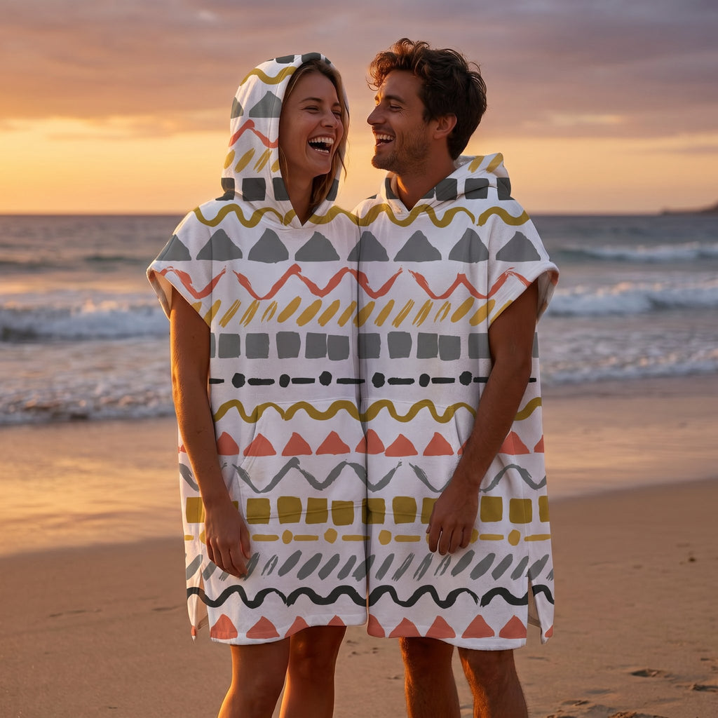 Poncho serviette à capuche motif zigzags graphiques porté par un couple souriant sur une plage au coucher du soleil.