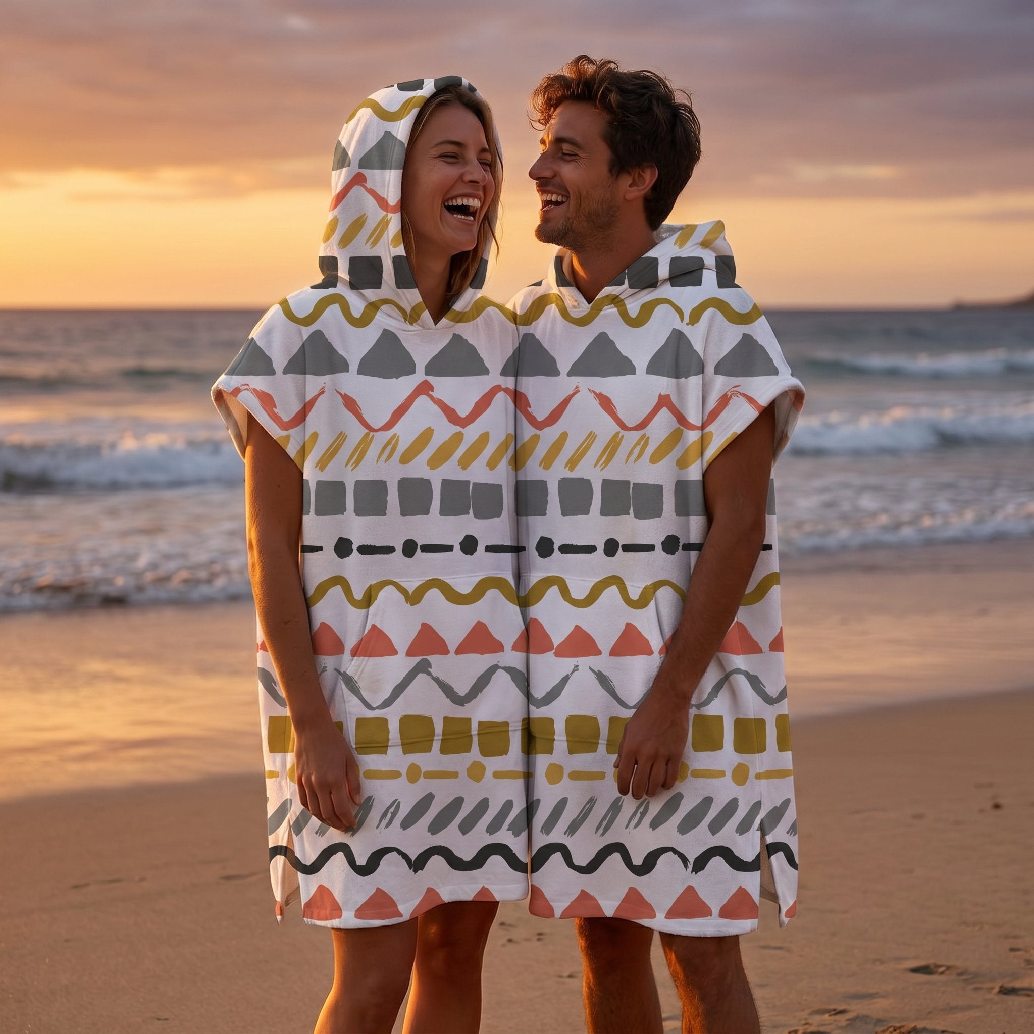 Poncho serviette à capuche motif zigzags graphiques porté par un couple souriant sur une plage au coucher du soleil.