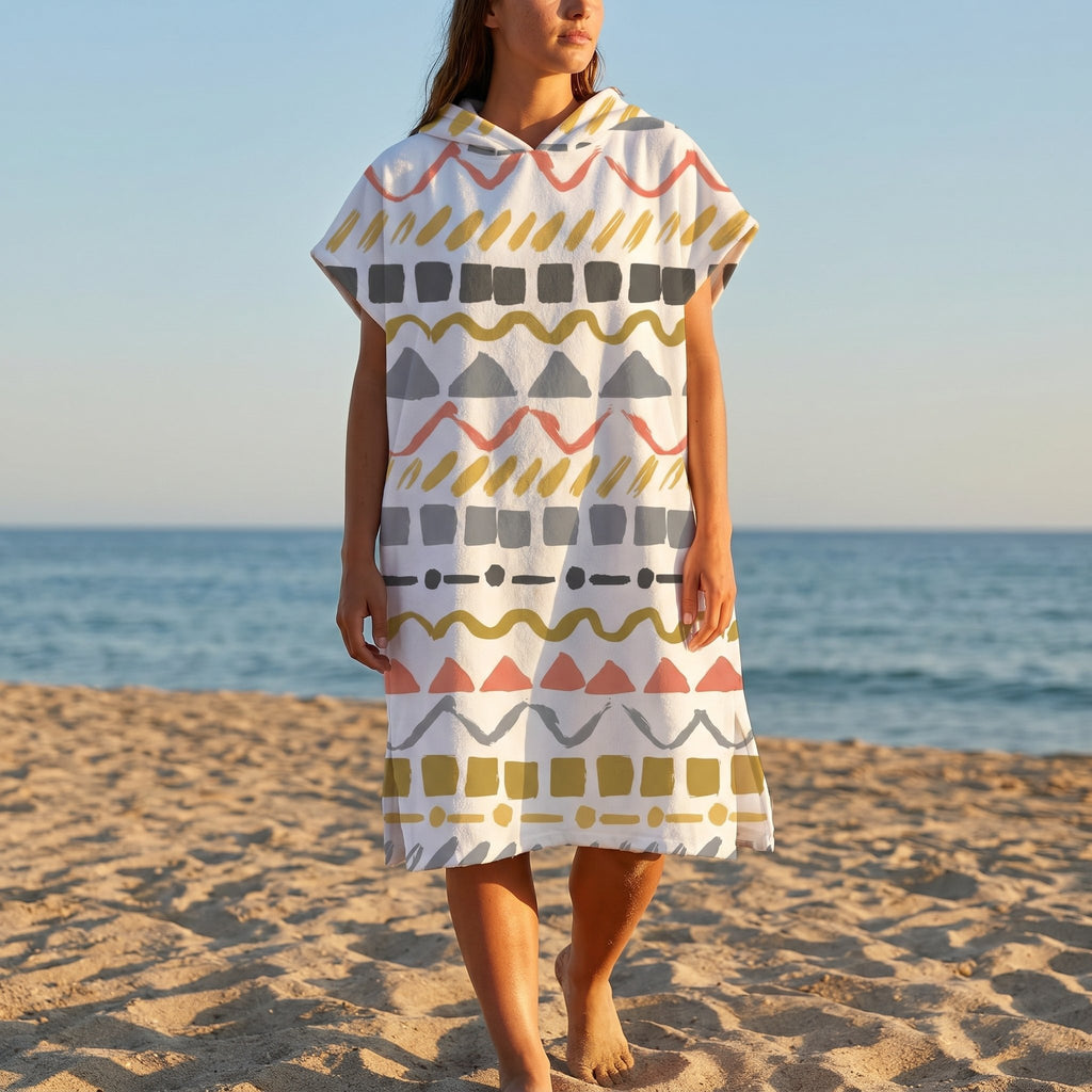Poncho serviette à capuche motif zigzags graphiques porté par une femme marchant sur le sable face à la mer.