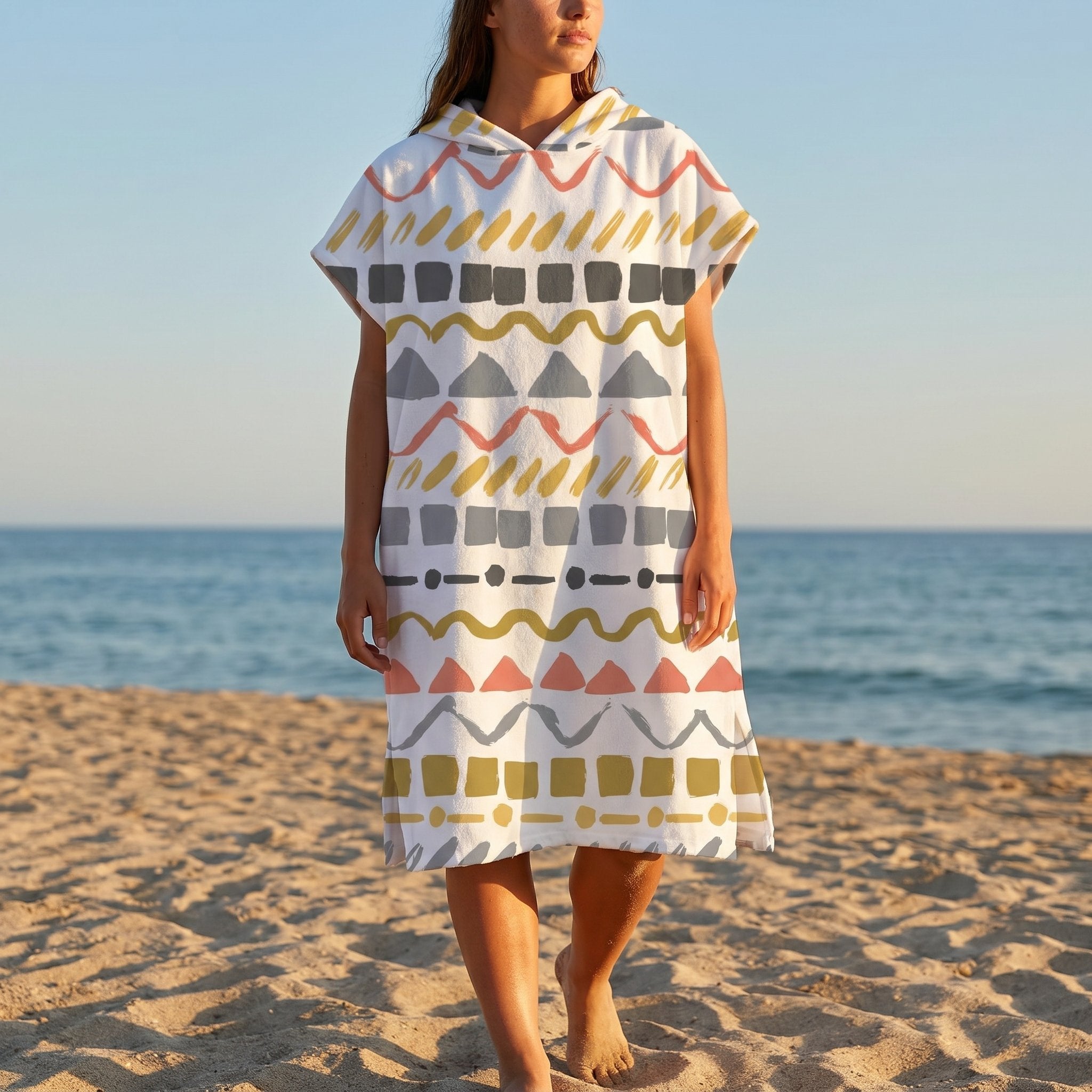 Poncho serviette à capuche motif zigzags graphiques porté par une femme marchant sur le sable face à la mer.
