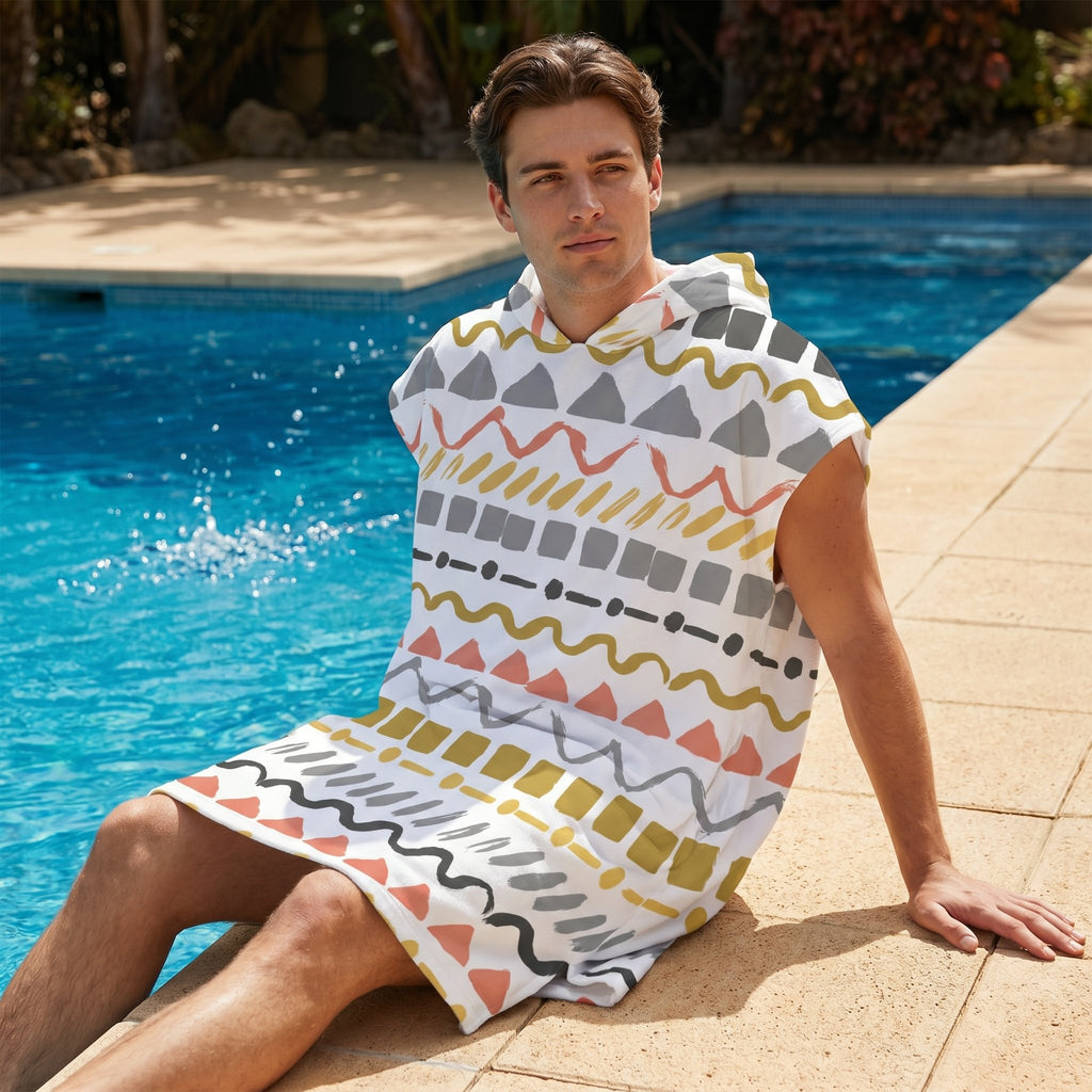 Poncho serviette à capuche motif zigzags graphiques porté par un homme assis au bord d'une piscine, les pieds dans l'eau.