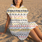 Poncho serviette à capuche motif zigzags graphiques porté par une femme assise sur le sable, vue de près.