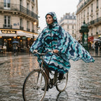 Poncho vélo à chevrons menthe, porté par une femme à vélo sous la pluie, vue de profil.