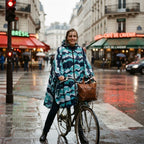 Poncho vélo à chevrons menthe, porté par une femme souriante à l'arrêt sur son vélo en ville.
