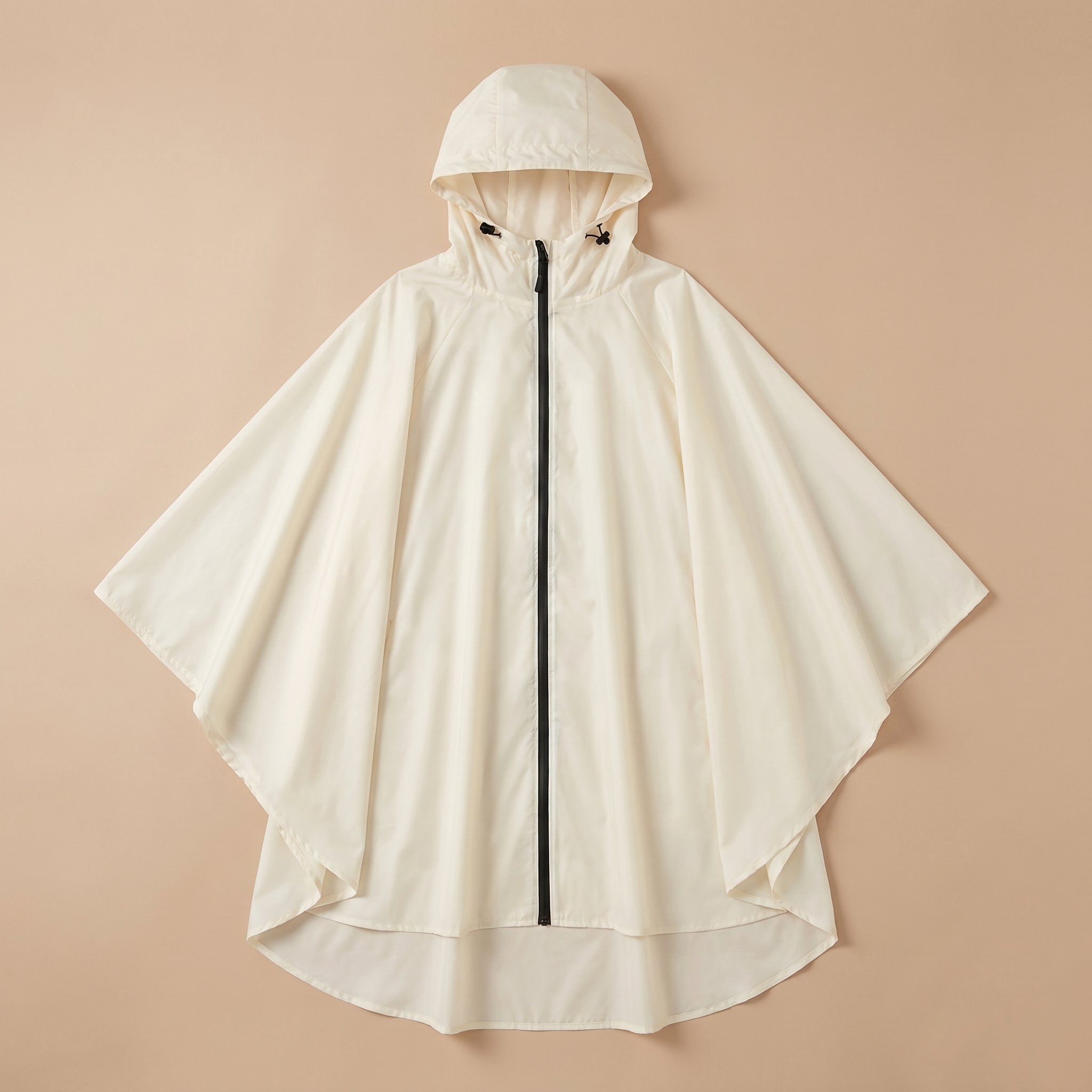 Poncho vélo crème uni, posé à plat sur un fond beige clair, montrant sa forme ample.
