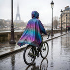 Poncho vélo irisé violet vu de dos sur une cycliste à vélo longeant un quai pluvieux.