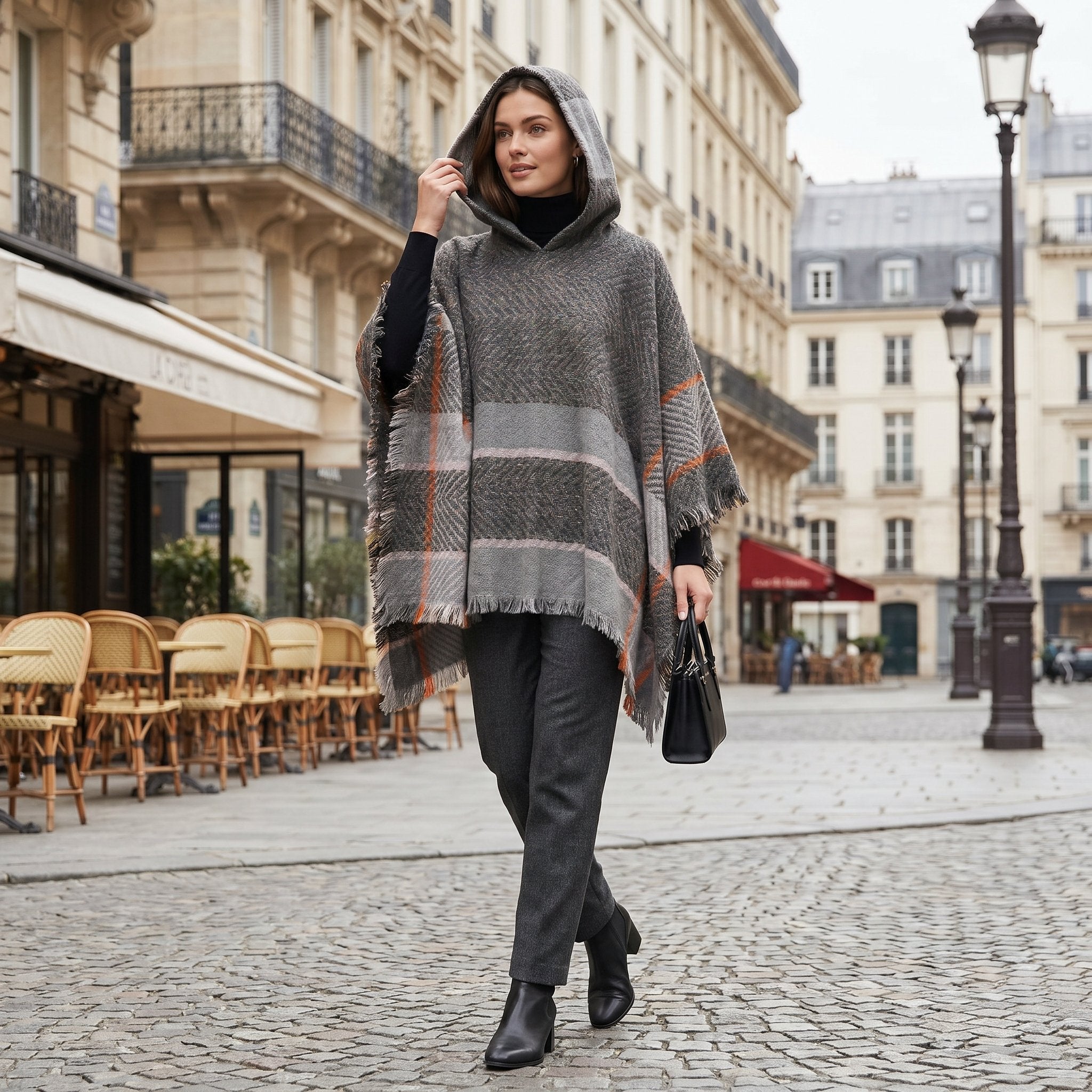 Pull poncho à capuche femme rayé gris, porté de face par une femme en ville. Il est gris avec des motifs à chevrons et des