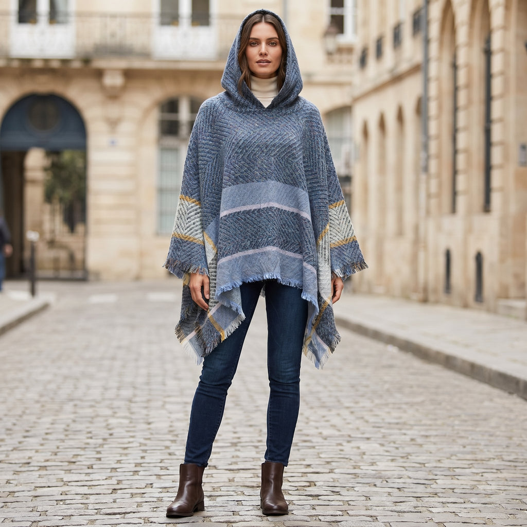 Pull poncho à capuche femme gris-bleu, porté de face par une femme en extérieur, révélant sa coupe ample et ses motifs